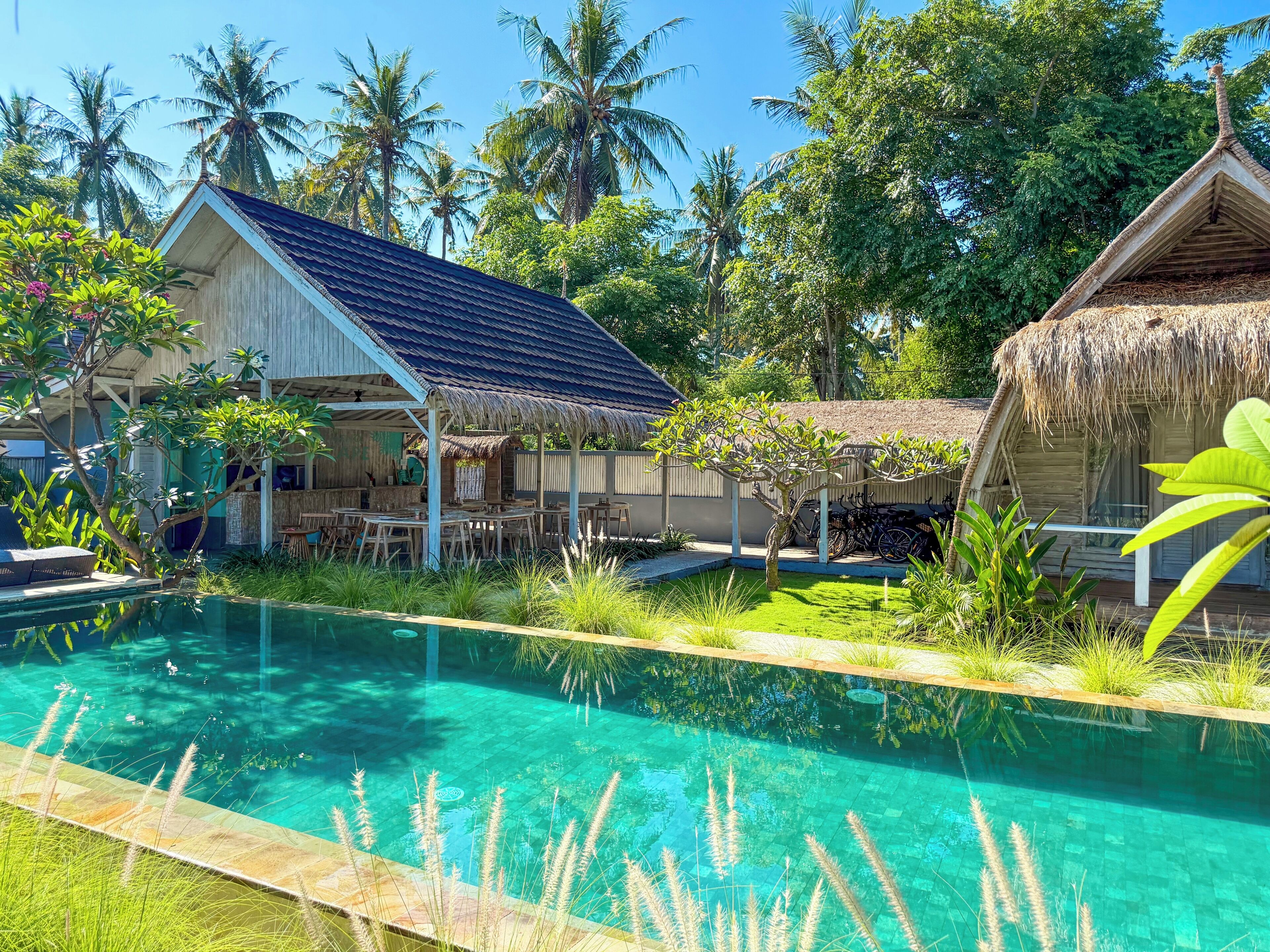 Una piscina de agua cristalina, rodeada de vegetación tropical y dos estructuras de madera con techos de paja.