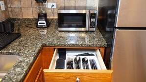 A kitchen with a microwave, blender, and drawer with utensils.