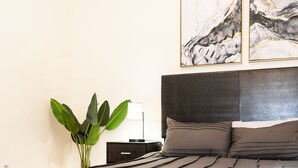 A modern bedroom with a large bed, a bedside table with a lamp, and a plant.