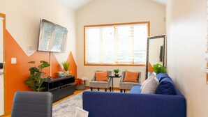 A living room with a blue sofa, two armchairs, a small table, and a large window with blinds.