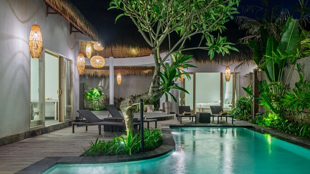 A poolside area with lounge chairs, a thatched roof, and ambient lighting. - Brand New Luxury 3BR Villa Ethnic Ubud 3 (Ubud)