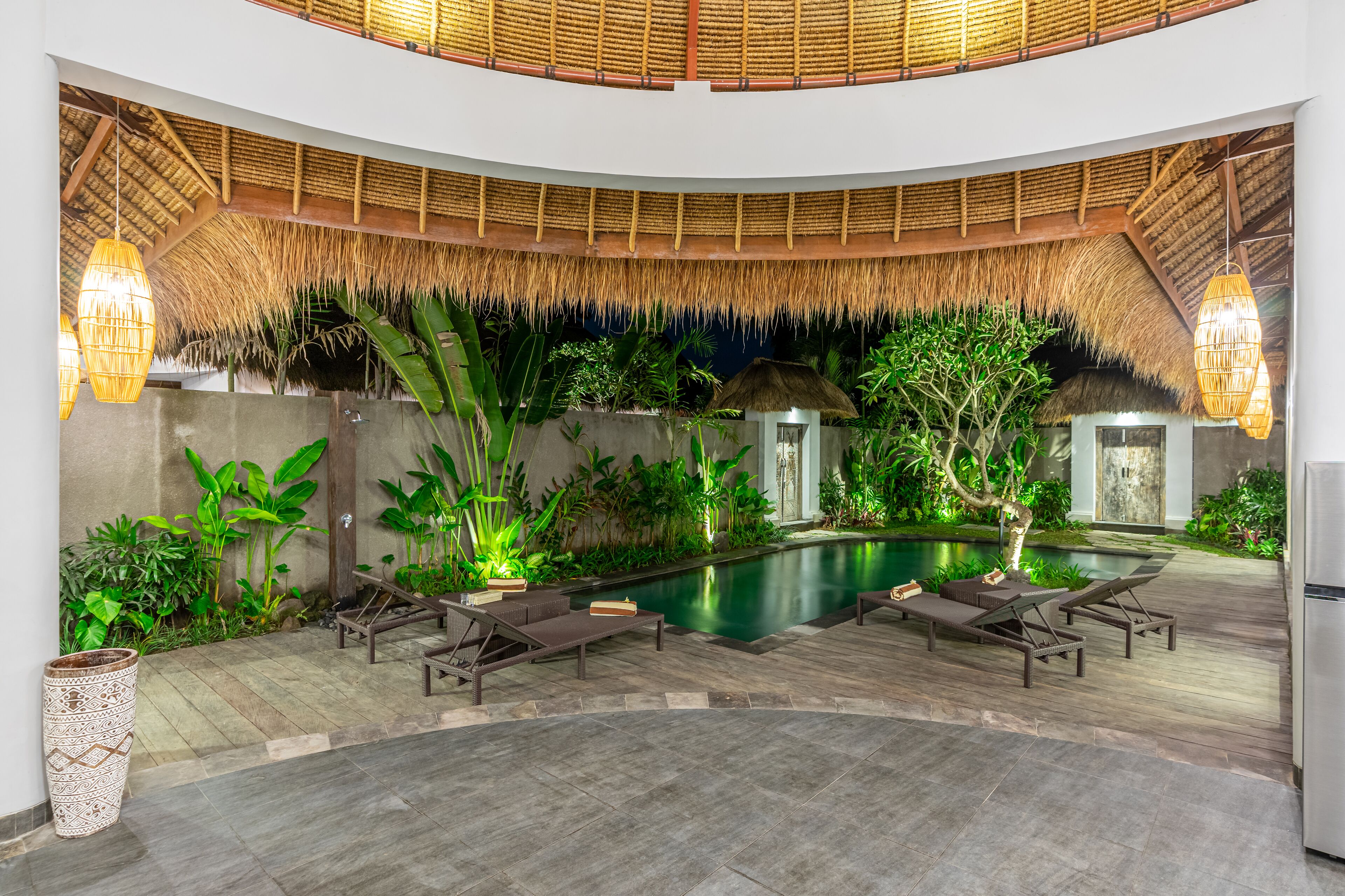 Un espace piscine doté de chaises longues, d’un toit de chaume et de plantes tropicales.