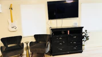 Una sala de estar con un mueble negro para centro de entretenimiento, dos sillas negras, una guitarra blanca y un televisor montado en la pared.