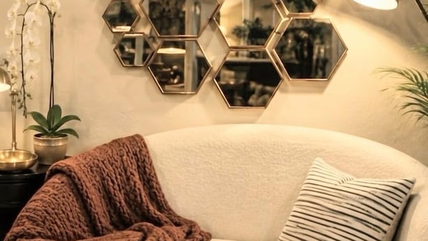 A living room with a beige sofa, a brown knitted blanket, a striped pillow, a round wooden coffee table, and a hexagonal mirror wall. - Charming Midtown Studio: Steps to Ice Blocks (Sacramento)