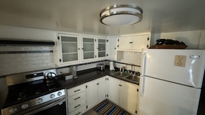 A compact kitchen with white cabinets, a stainless steel stove, a refrigerator, and a tiled backsplash. - Charming Midtown Studio: Steps to Ice Blocks (Sacramento)