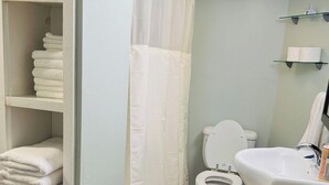 Kylpyhuoneessa on wc, pesuallas ja suihkuverho. Siellä on myös hyllyjä, joilla on pyyhkeitä, ja pieni matto lattialla.