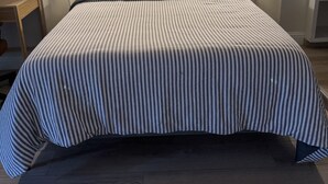 A neatly made bed with striped bedding, a framed picture of a bridge on the wall, and bedside lamps on either side. - Charming Midtown Studio: Steps to Ice Blocks (Sacramento)