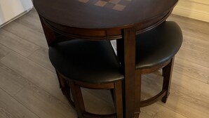 A round wooden dining table with a checkered tablecloth, two black upholstered chairs, and a window with blinds in the background. - Charming Midtown Studio: Steps to Ice Blocks (Sacramento)