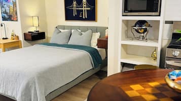 Una habitación de hotel con cama, escritorio, lámpara, un cuadro, un globo terráqueo y microondas.