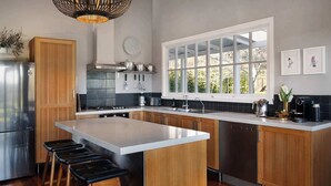 Eine moderne Küche mit Kochinsel, Holzschränken, Edelstahlgeräten und einem großen Fenster, das für natürliches Licht sorgt.