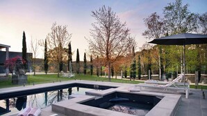 Ein Poolbereich mit zwei Whirlpools, Liegestühlen und einer Pergola mit Sonnenschirm.