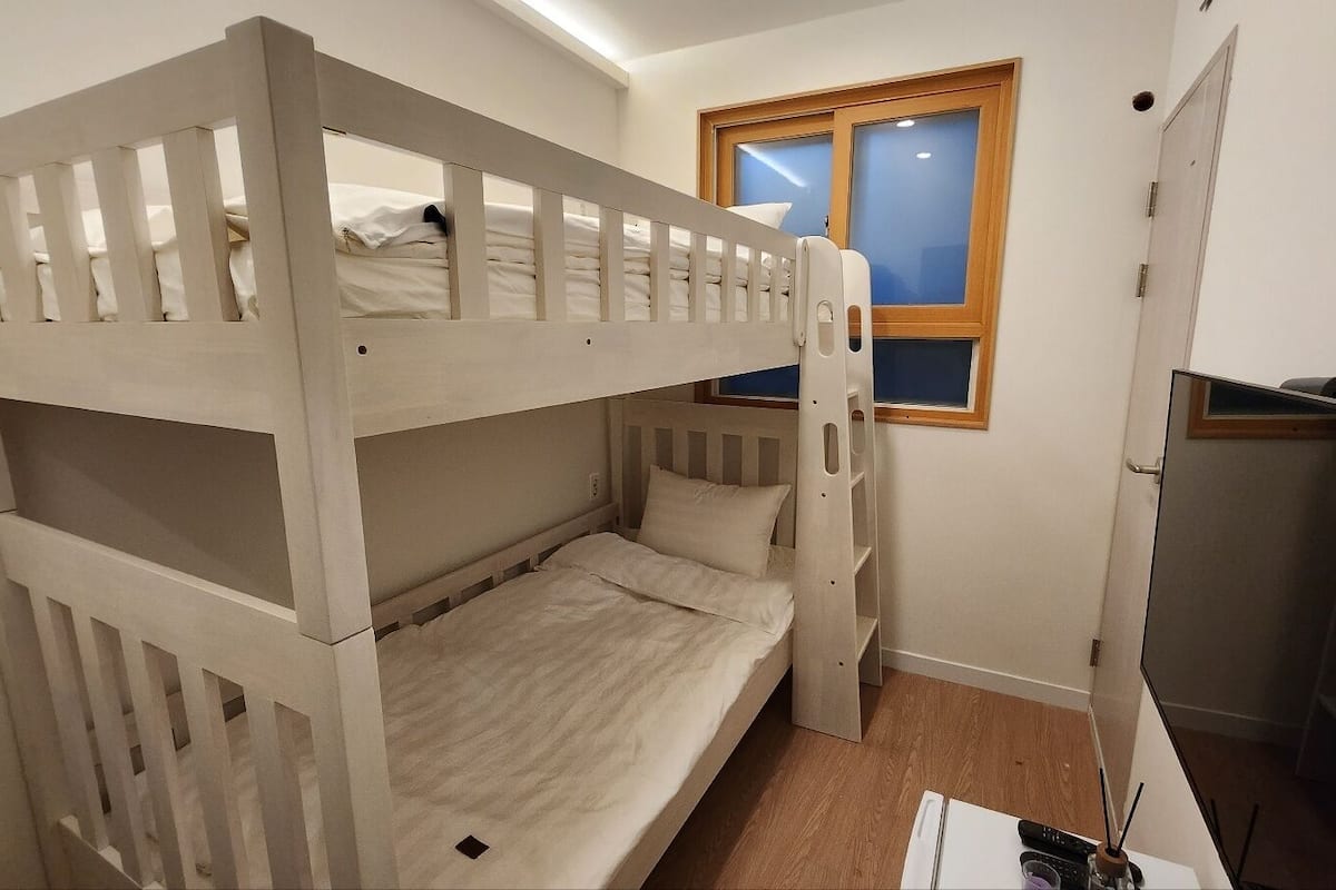 A bunk bed room with a wooden frame, a small window, and a door.
