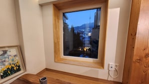 Una stanza con pavimento in legno, una piccola finestra che si affaccia su edifici e un quadro appeso al muro.