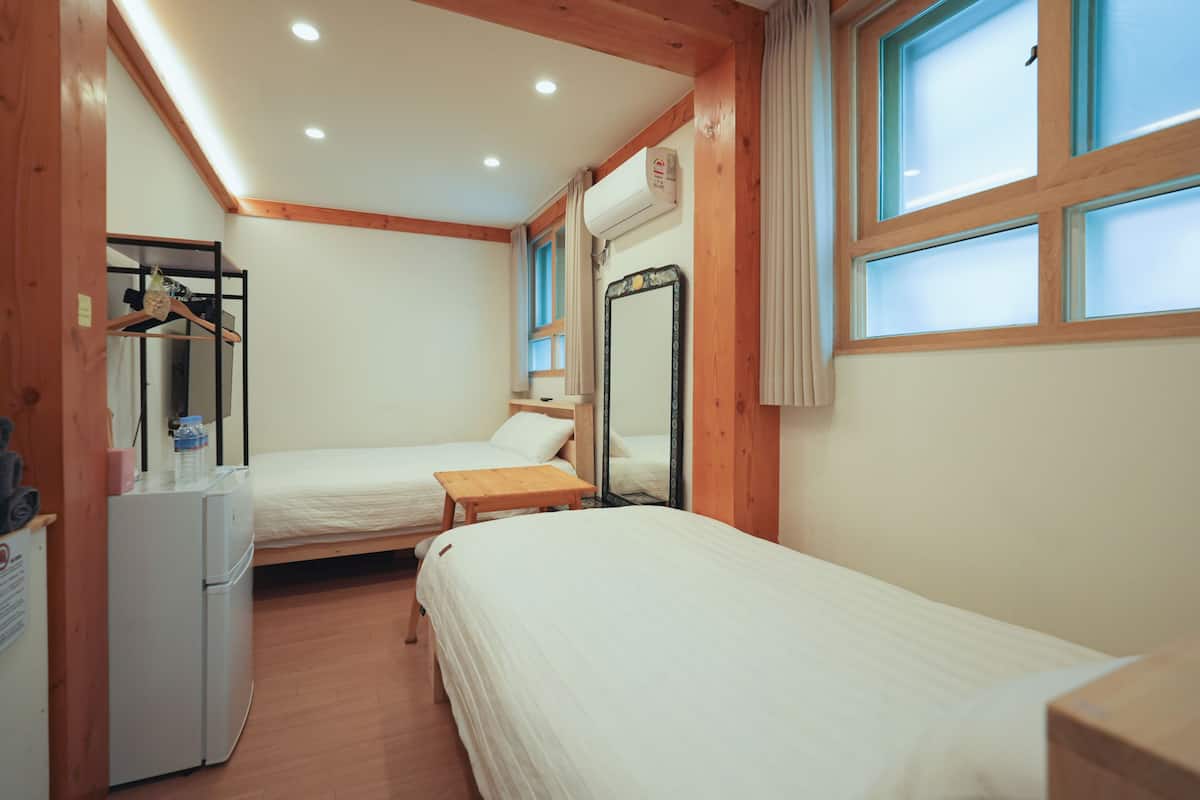 A room with two beds, a wooden desk, a mirror, and a refrigerator.