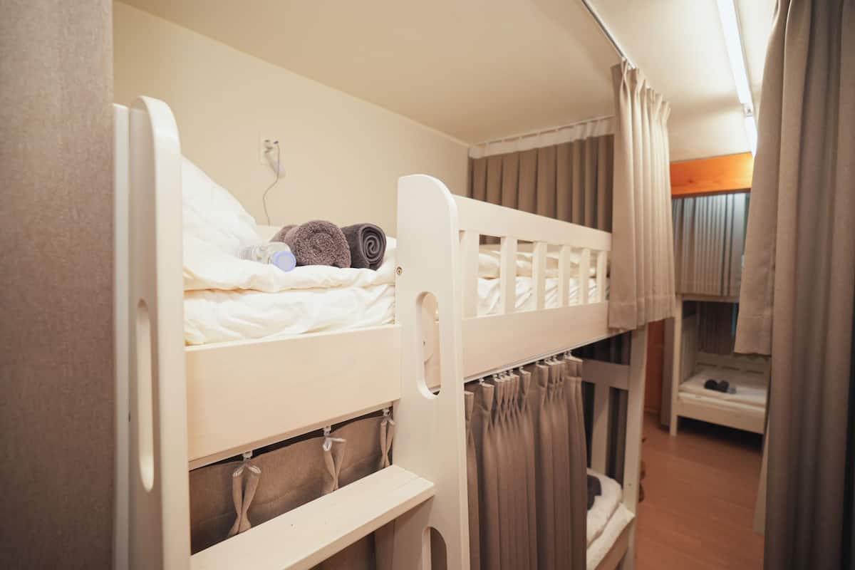 A bunk bed with a white headboard, a bedside table with a lamp, and a curtain.