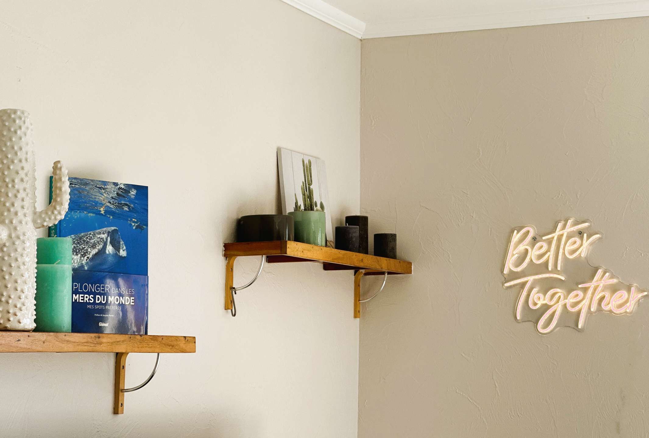 A room with a beige wall, a neon sign saying "Better Together", and two wooden shelves with various items.