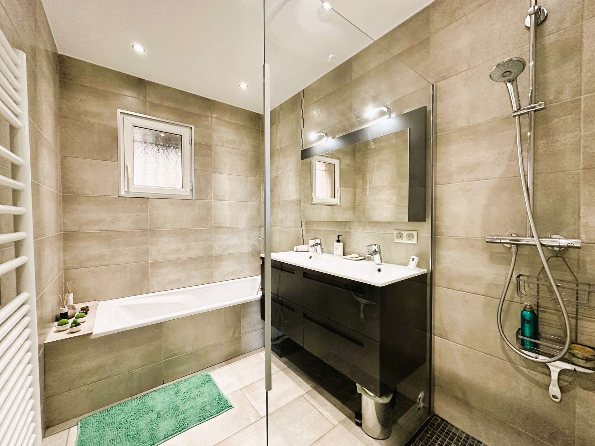 A modern bathroom with a glass shower enclosure, a bathtub, and a vanity with a mirror.