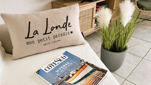 A beige pillow with French text, a magazine, and a potted plant on a white surface.