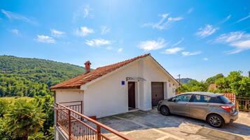 A single-story building with a red-tiled roof, a car parked in front, and a view of green hills in the background.