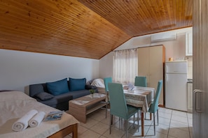 Una habitación compacta con techo de madera, un sofá, una mesa de comedor con sillas, una cama y una kitchenette.
