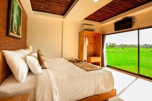 A bedroom with a bed, a wooden wardrobe, a large window with a view of a green field, and a painting on the wall. - Ubud 3BD Premium Villa: pool and pristine views! (Ubud)