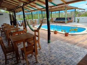 A covered outdoor area with wooden tables and chairs, a pool, and hammocks. - Panoramic Rooms at Galapagos Verde Azul (Puerto Ayora)
