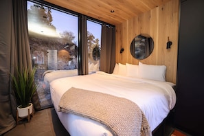 Une chambre avec un grand lit, une plante en pot, un miroir et une vue sur lâextĂ©rieur.