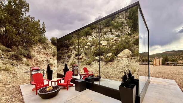 Un espace extérieur moderne, aménagé avec des chaises rouges, un barbecue et un grand miroir qui reflète le paysage environnant.