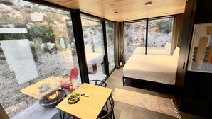 Une chambre moderne avec un plafond en bois, de grandes fenêtres, un lit, une table avec un saladier de légumes verts et un foyer.