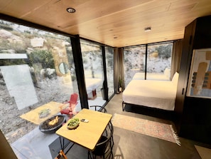 Una habitación moderna con techo de madera, ventanas amplias, cama, mesa con un cuenco de verduras y una chimenea.