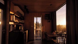Une cuisine compacte avec un coin repas, des murs en bois et une vue sur l’extérieur grâce à une porte vitrée.