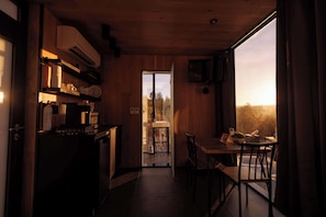 A compact kitchen with a dining area, wooden walls, and a view through a glass door.