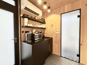 A compact kitchen with a microwave, coffee maker, and shelves with dishes.