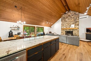 Una cocina moderna con chimenea de piedra, techo de madera y una isla grande con armarios negros.