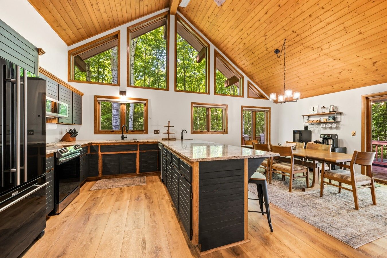 A modern kitchen with a central island, wooden cabinets, and large windows.