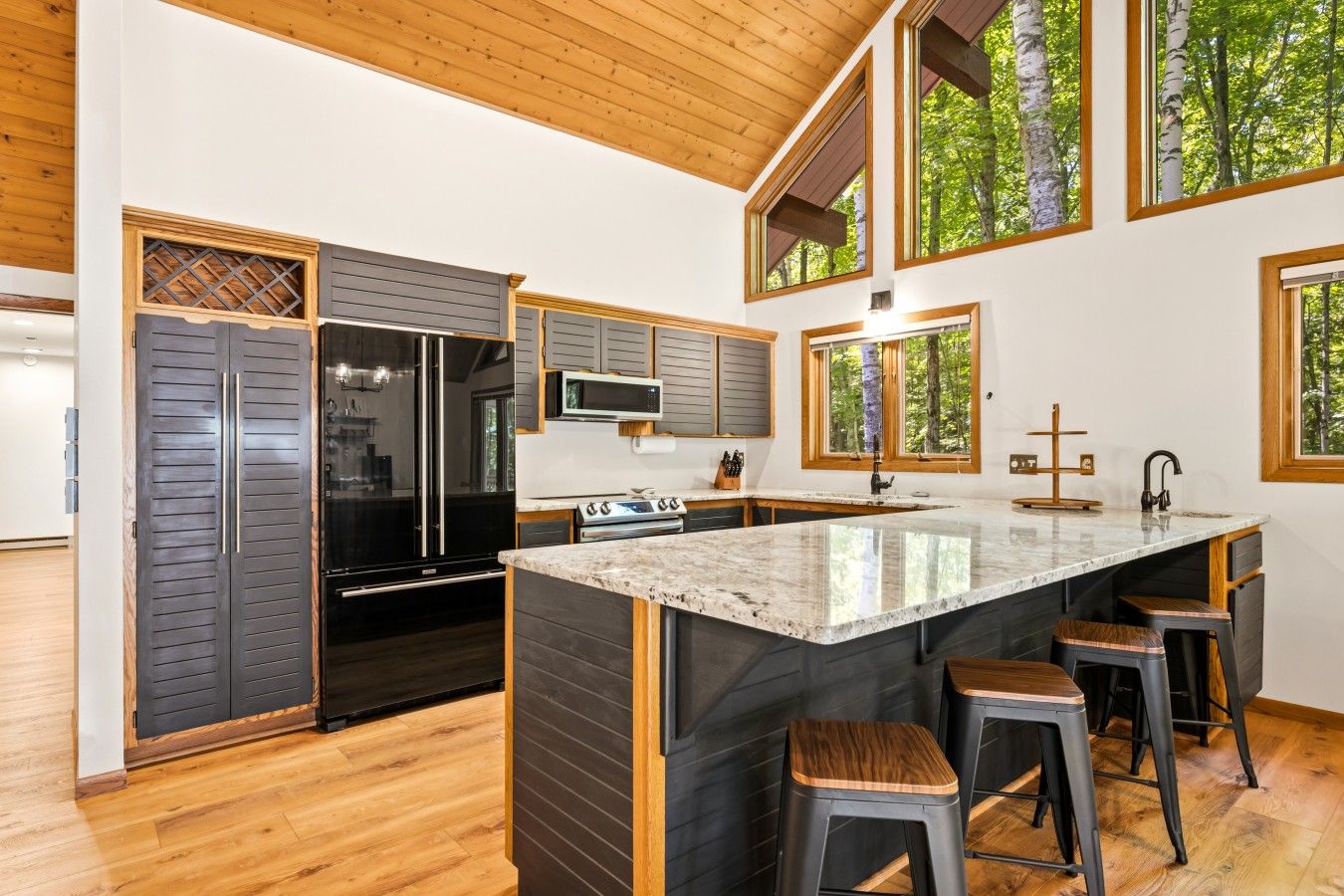 A modern kitchen with a central island, wooden flooring, and large windows.