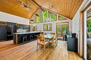 A modern kitchen with a central island, wooden dining table, and large windows.