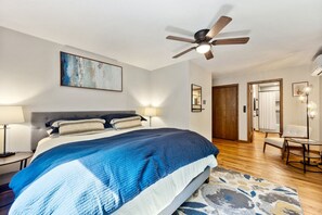 Un dormitorio con una cama, un ventilador de techo, un cuadro, una puerta y una lámpara.