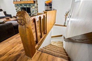 Een houten trap met een beeldhouwsel van een leeuwenkop, een stenen openhaard en een moderne keukenhoek.