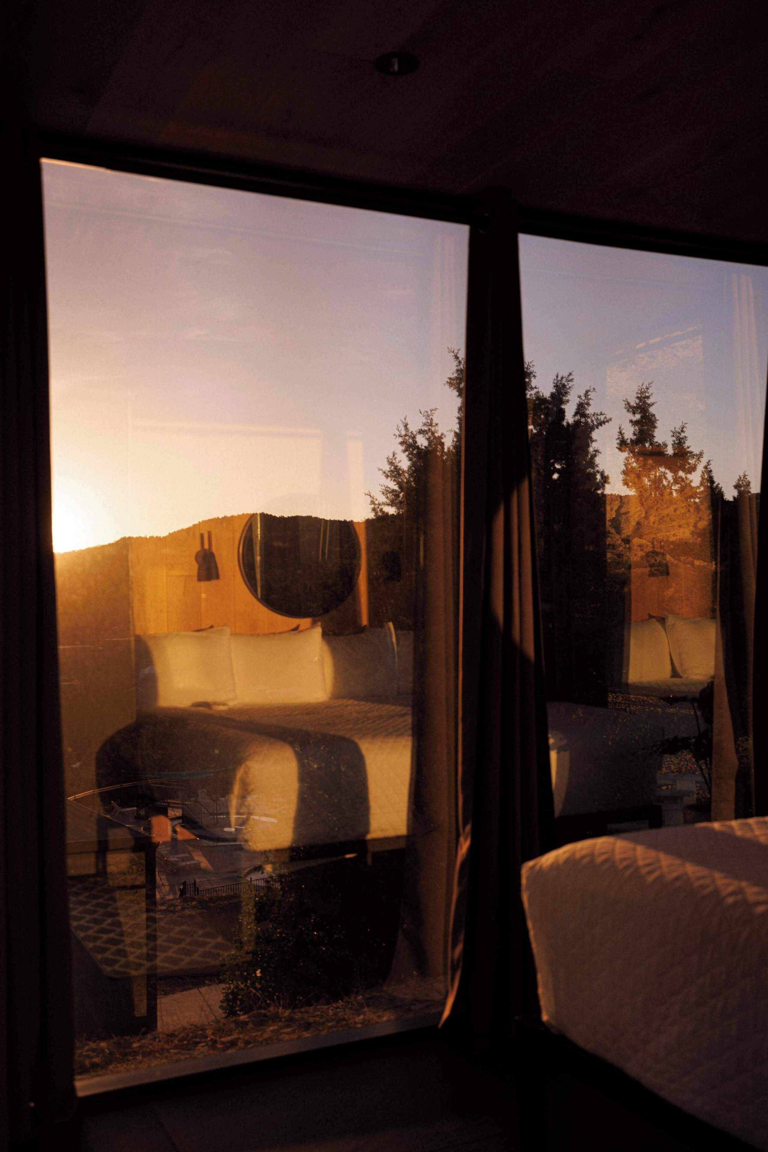 A room with a bed, a sofa, and a large window with a view of trees and a building.