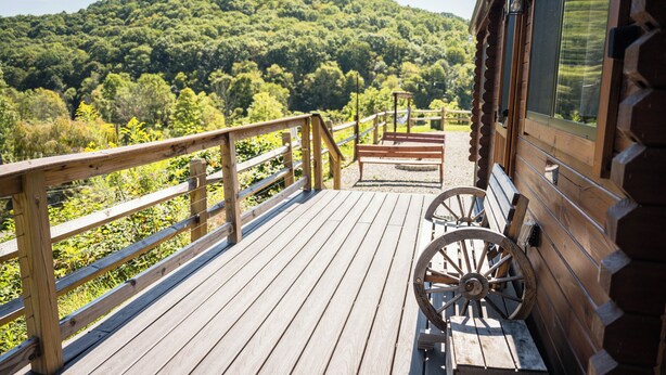 A wooden deck with a wooden bench and a wagon wheel, overlooking a forested hillside.