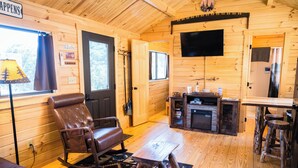 A cozy cabin interior with a leather recliner, a small wooden table, a TV mounted on the wall, and a rustic wooden bar area.