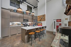 A modern kitchen with a central island, bar stools, and a vintage coffee machine.