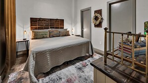 A bedroom with a large bed, a bookshelf, a small table, and a decorative wreath on the wall. - Waco Memory Lane, Downtown Luxury Loft- Steps to Silos/Baylor/McLane (Waco)
