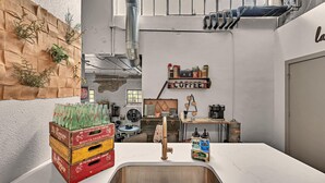 A kitchen with a white countertop, stainless steel sink, and a shelf with coffee and spices. - Waco Memory Lane, Downtown Luxury Loft- Steps to Silos/Baylor/McLane (Waco)