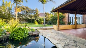 A koi pond with a stone pathway leading to a covered patio area. - Classic Hampton Retreat (Hampton)