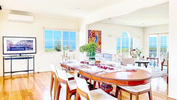A spacious dining area with a large round table, multiple chairs, and a television on a stand. - Classic Hampton Retreat (Hampton)