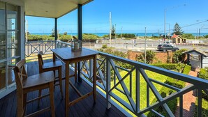 A balcony with a wooden table and chairs, overlooking a road with a car and a pedestrian crossing. - Classic Hampton Retreat (Hampton)