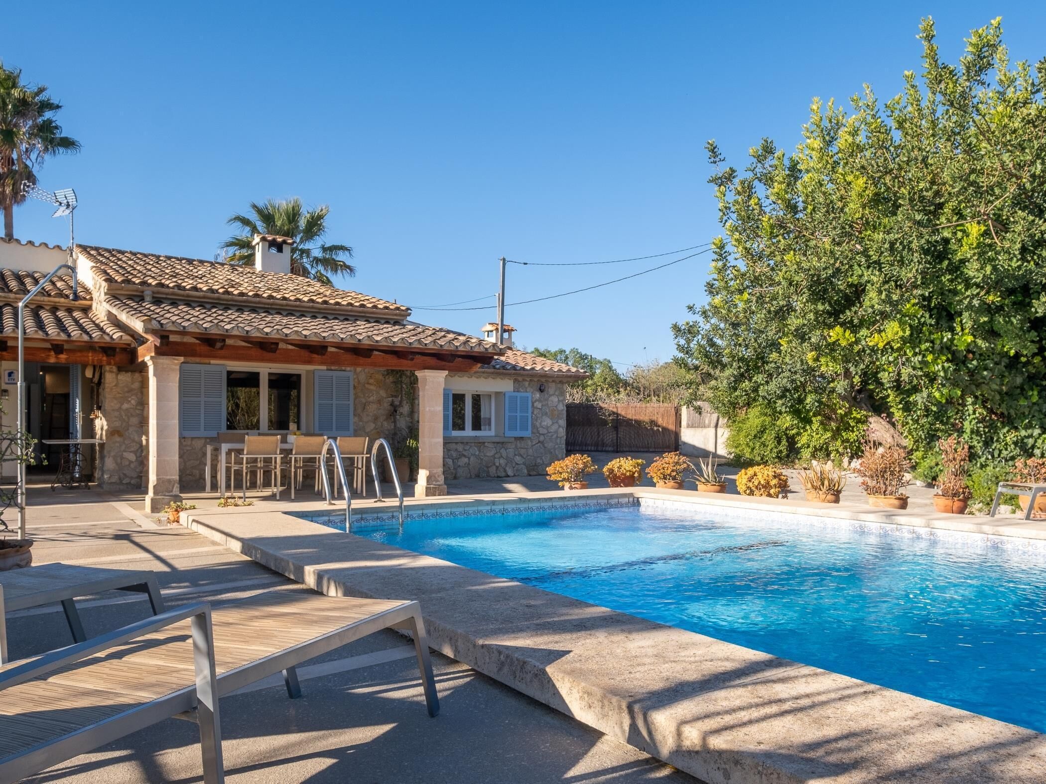 A pool area with a stone house, outdoor seating, and potted plants.