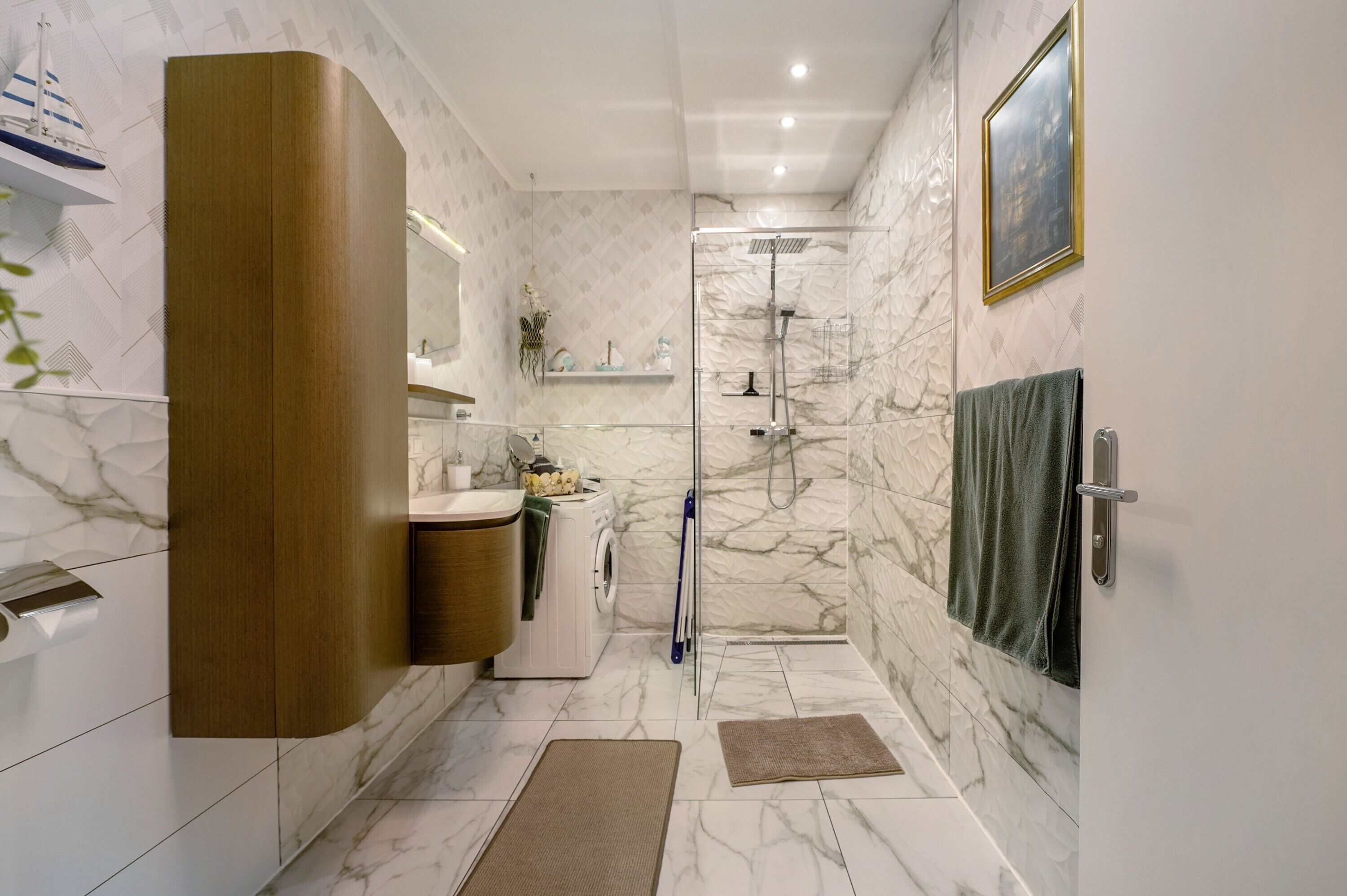 A bathroom with a marble wall, a wooden cabinet, a washing machine, and a shower.
